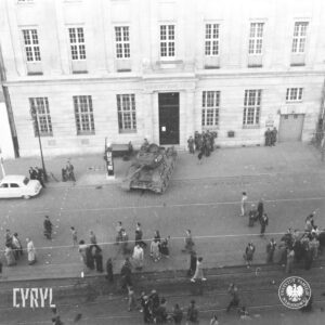 czołg stojący przed okazałym budynkiem, pod ścianą budynku kilku żołnierzy wokół pojedynczy ludzie