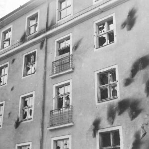 fragment elewacji pięciokondygnacyjnego budynku, ciemne ślady po obrzuceniu budynku palącymi się butelkami z benzyną, powybijane szyby
