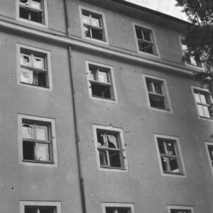 fragment elewacji pięciokondygnacyjnego budynku, ślady po pociskach, powybijane szyby