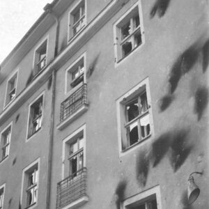 fragment elewacji pięciokondygnacyjnego budynku, ciemne ślady po obrzuceniu budynku palącymi się butelkami z benzyną, powybijane szyby