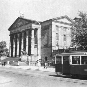 tramwaje jadące ulicą, w głębi okazały gmach z portykiem i kolumnami, pojedynczy przechodnie