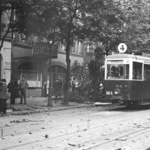 tramwaj z wybitymi szybami stoi na ulicy, w głębi kamienica z murowanym balkonem