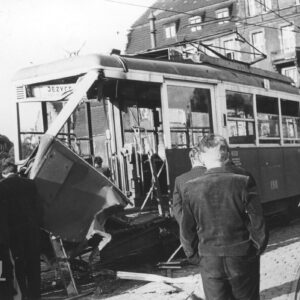 tramwaj z wybitymi szybami i rozbitym przodem, przy nim stoi kilka osób, w głębi okazały budynek