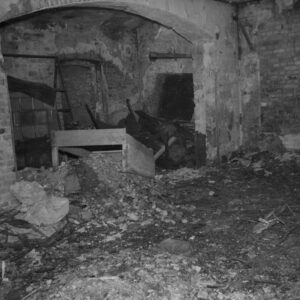pomieszczenie w przyziemiu, na podłodze gruz i rozbite meble lub drewniane skrzynie