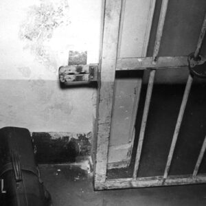  ściana z drzwiami zamkniętymi metalową sztabą, nad drzwiami widoczny fragment propagandowego hasła