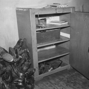 otwarta metalowa szafa z wyłamanym zamkiem, z lewej sterta butów leżąca na podłodze