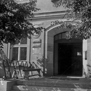 wejście do budynku, na elewacji, po obu stronach drzwi tablice informacyjne i godło