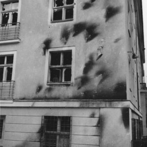 fragment elewacji pięciokondygnacyjnego budynku, ciemne ślady po obrzuceniu budynku palącymi się butelkami z benzyną, powybijane szyby