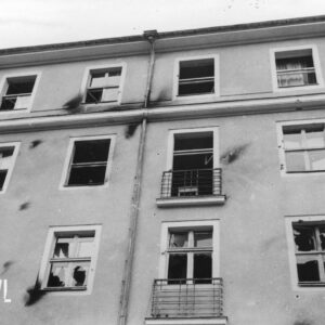 fragment elewacji pięciokondygnacyjnego budynku, ciemne ślady po obrzuceniu budynku palącymi się butelkami z benzyną, powybijane szyby