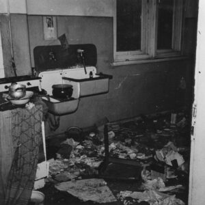 wnętrze zdemolowanej kuchni, na podłodze porozrzucane rzeczy, z lewej piec, pośrodku zlewozmywak, z prawej okno