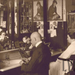 mężczyzna i kobieta siedzący na fotelach w zakładzie fryzjerskim; obok kobiety stoi strzygący ją mężczyzna w fartuchu fryzjerskim