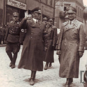 grupa mężczyzn w mundurach niemieckich, maszerująca środkiem brukowanej ulicy, na czele dwóch mężczyzn w długich płaszczach i czapkach oficerskich