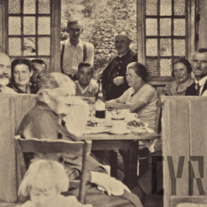 grupa ludzi w różnym wieku siedząca i stojąca przy zastawionym stole, w oddali widać ogród