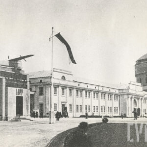 z lewej niewielki pawilon zwieńczony modelem samolotu, przed nim maszt z flagą, w głębi dwukondygnacyjny pawilon o monumentalnej, klasycznej architekturze, zwieńczony attyką oraz fragment masywnej, okrągłej wieży