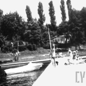 brzeg jeziora z pomostem, na nim kilka osób, w głębi zadrzewiony brzeg