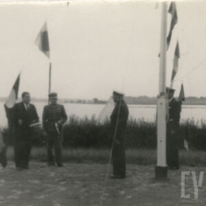 kilka osób stoi na brzegu jeziora, w ziemi maszty z proporcami