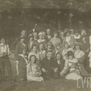 grupa kobiet i mężczyzn, kilkoro z instrumentami w rękach, pozuje do fotografii na leśnej polanie, w tle drzewa