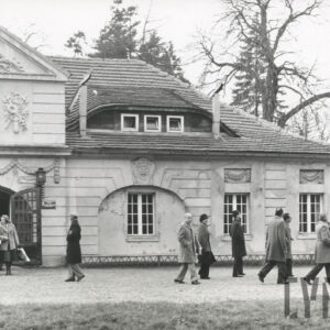 parterowy, okazały budynek z ozdobną fasadą i trójkątnym szczytem i zegarem, z budynku wychodzi kilkanaście osób