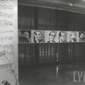 sala wystawowa, w niej zaprezentowane zdjęcia w dużych formatach, głównie portrety muzyków grających na skrzypcach, na tle ciemnej tkaniny, z lewej fragment zapisu nutowego utworu