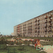 matka z dzieckiem na ławce na placu zabaw; w głębi trawnik, kwiaty, huśtawki i bloki z wielkiej płyty