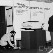 dwóch mężczyzn montujących sprzęt elektroniczny na tle ścianki z napisami w języku polskim