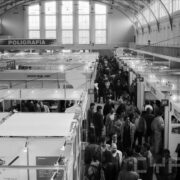 tłum ludzi przechodzący między stoiskami rozlokowanymi w dużej hali o półokrągłym suficie