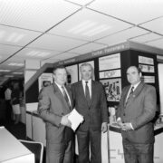 trzech mężczyzn w średnim wieku w garniturach stojących na tle stoiska z narzędziami