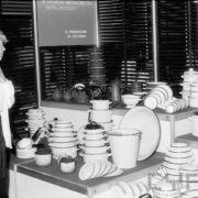 kobieta przyglądająca się garnkom, pokrywkom i czajnikom ustawionym na podeście