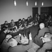 grupa mężczyzn i kobiet siedząca przy stołach, na stołach szklanki, kieliszki, butelki i talerze