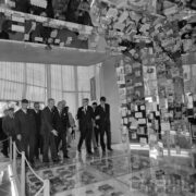 grupa mężczyzn w hali wystawowej stoi na szklanej podłodze, pod szkłem równo poukładane pudełka