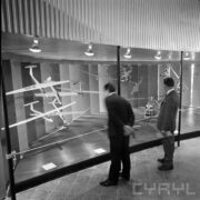 stoisko z modelami śmigłowców i szybowców w pawilonie wystawowym, przy nim stoi dwóch mężczyzn