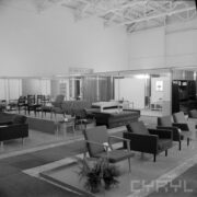 stoiska z fotelami tapicerowanymi, w głębi łóżka i kanapy w hali wystawowej