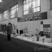 stoiska w hali wystawowej, przed nimi stoi jeden mężczyzna w płaszczu