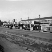 stoisko z maszynami i urządzeniami pod zadaszoną wiatą wystawową, na pierwszym planie betonowy plac, pośrodku tory kolejowe