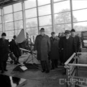 grupa mężczyzn w płaszczach oraz nakryciach głowy w hali wystawowej