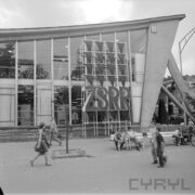 przeszklony budynek, przed nim duży napis ZSRR, zwiedzający ludzie, część z z nich siedzi na ławkach przed budynkiem