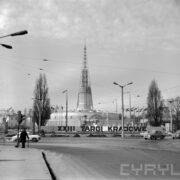 fragment ulicy z torowiskiem tramwajowym, w głębi budynek targowy, zwany Iglicą, przed nim duży napis reklamujący odbywające się targi, z lewej i prawej, jadące samochody