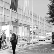 przeszklona hala wystawowa, przed nią samochody osobowe i spacerujący ludzie