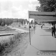 fragment asfaltowej alei wokół jeziora, fragment jeziora z lewej, spacerujący ludzie, w poprzek drogi rozstawione płachty materiału z napisami, w głębi budynek ze skośnym dachem