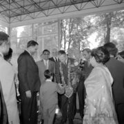 dwie kobiety i grupa mężczyzn w pawilonie wystawowym, w środku jeden z mężczyzn otrzymuje bukiet kwiatów od chłopca