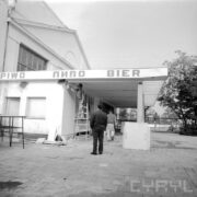 fragment otynkowanego budynku, jeden mężczyzna stoi na drabinie i maluje ścianę, dwóch stoi