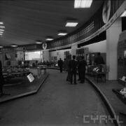 stoiska w pawilonie wystawowym, między nimi zwiedzający ludzie