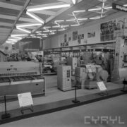 stoisko z urządzeniami w hali wystawowej, między nimi zwiedzający ludzie