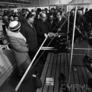 grupa kobiet i mężczyzn w płaszczach oglądają stoisko z butami w hali targowej