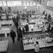 stoiska wystawowe z butami w hali targowej, pomiędzy stoiskami chodzą kobiety i mężczyźni