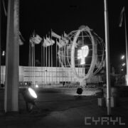 ażurowy model kuli ziemskiej z literką P w środku podświetloną neonem, w głębi maszty z flagami państw