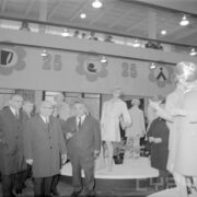 kilku mężczyzn w płaszczach w hali wystawowej ogląda ubrane manekiny