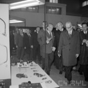 grupa mężczyzn, część w płaszczach w hali wystawowej
