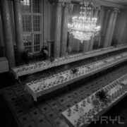 pomieszczenie z kolumnami i wysokimi oknami, u góry wiszący kryształowy żyrandol, z góry widoczne trzy rzędy zastawionych, długich stołów