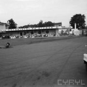 wybetonowany plac, pośrodku tory kolejowej, w głębi stoisko z maszynami pod zadaszoną wiatą wystawową